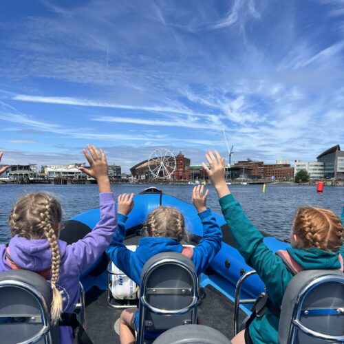 Three children sat on a boat with hands in the air enjoying themselves on a Children's Party trip