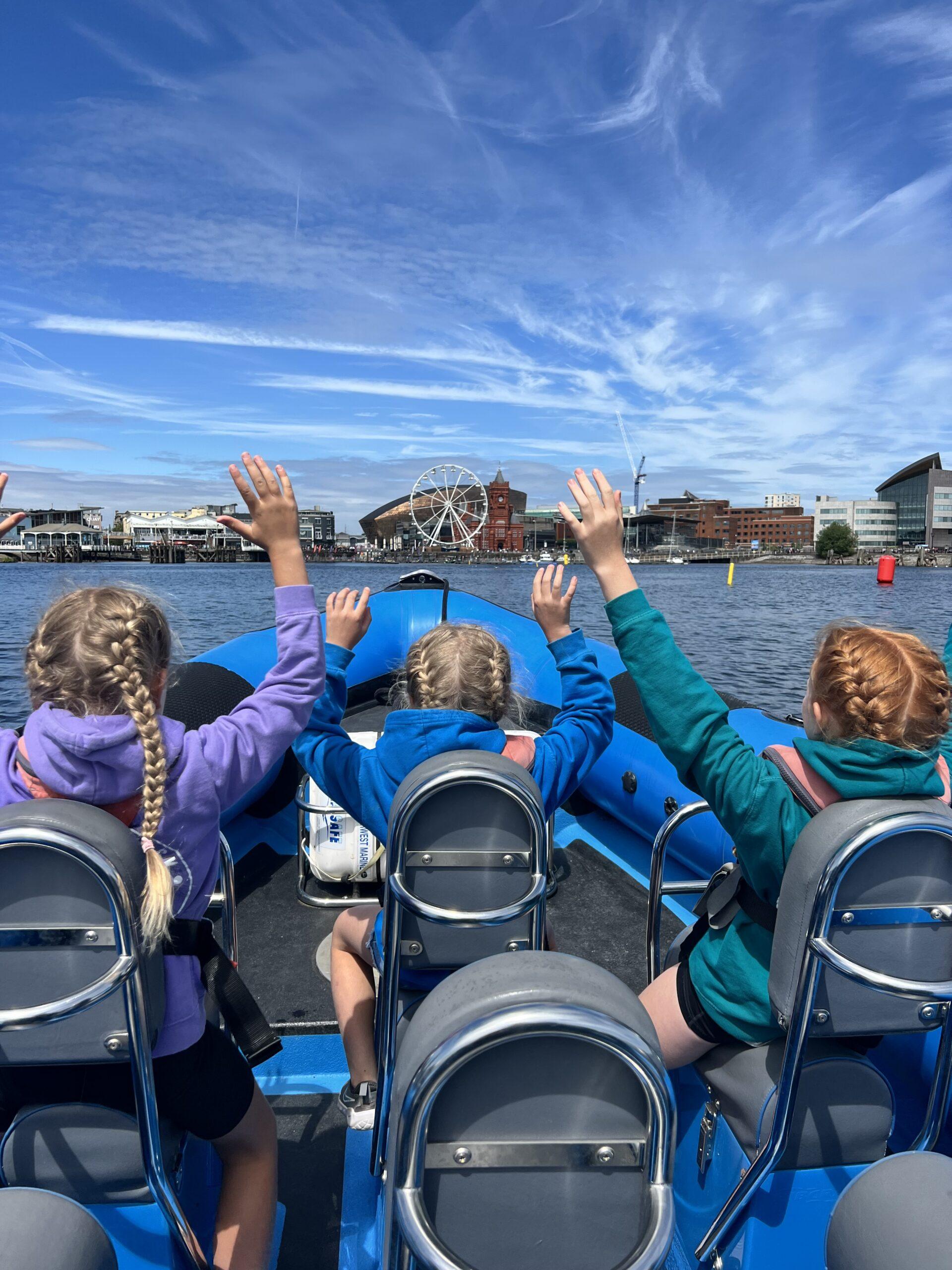 Three children sat on a boat with hands in the air enjoying themselves on a Children's Party trip